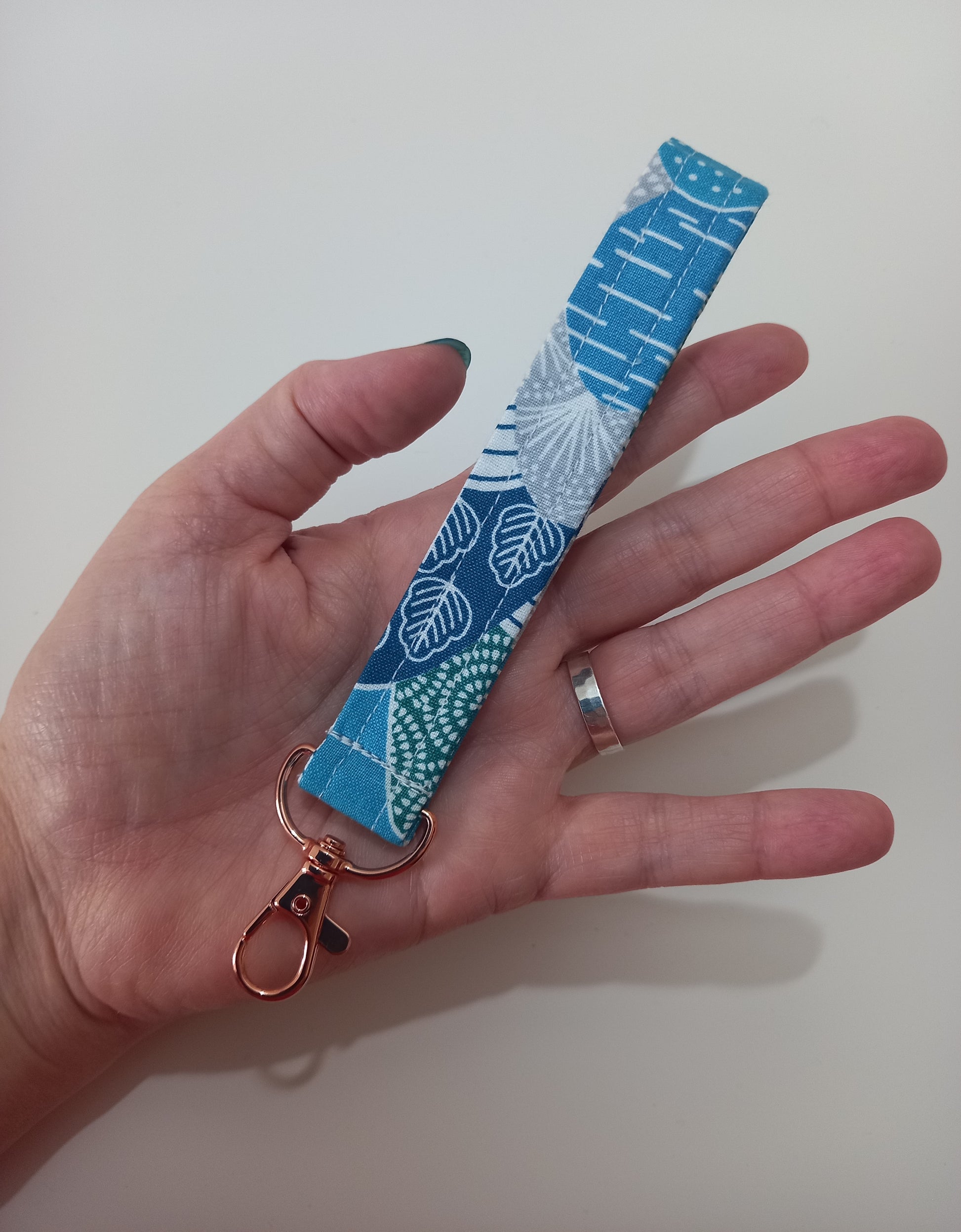 Our fabric wristlet in a lovely blue fabric with retro mountain pattern with sewn in rose gold keyfob. It's lying on the palm of a lady's open hand to show size comparison.